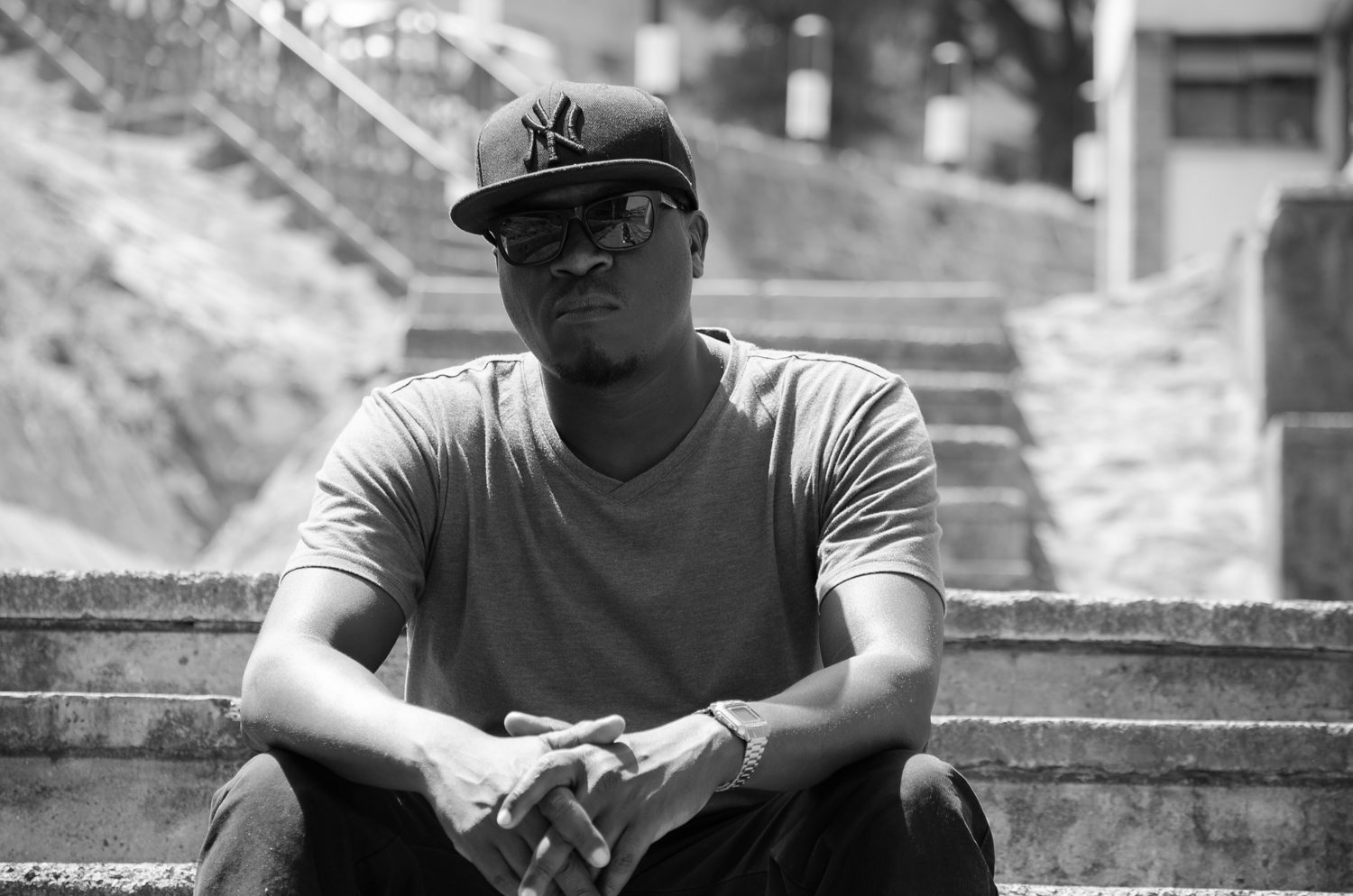 Solodified seated on outdoor stairs, cap and sunglasses