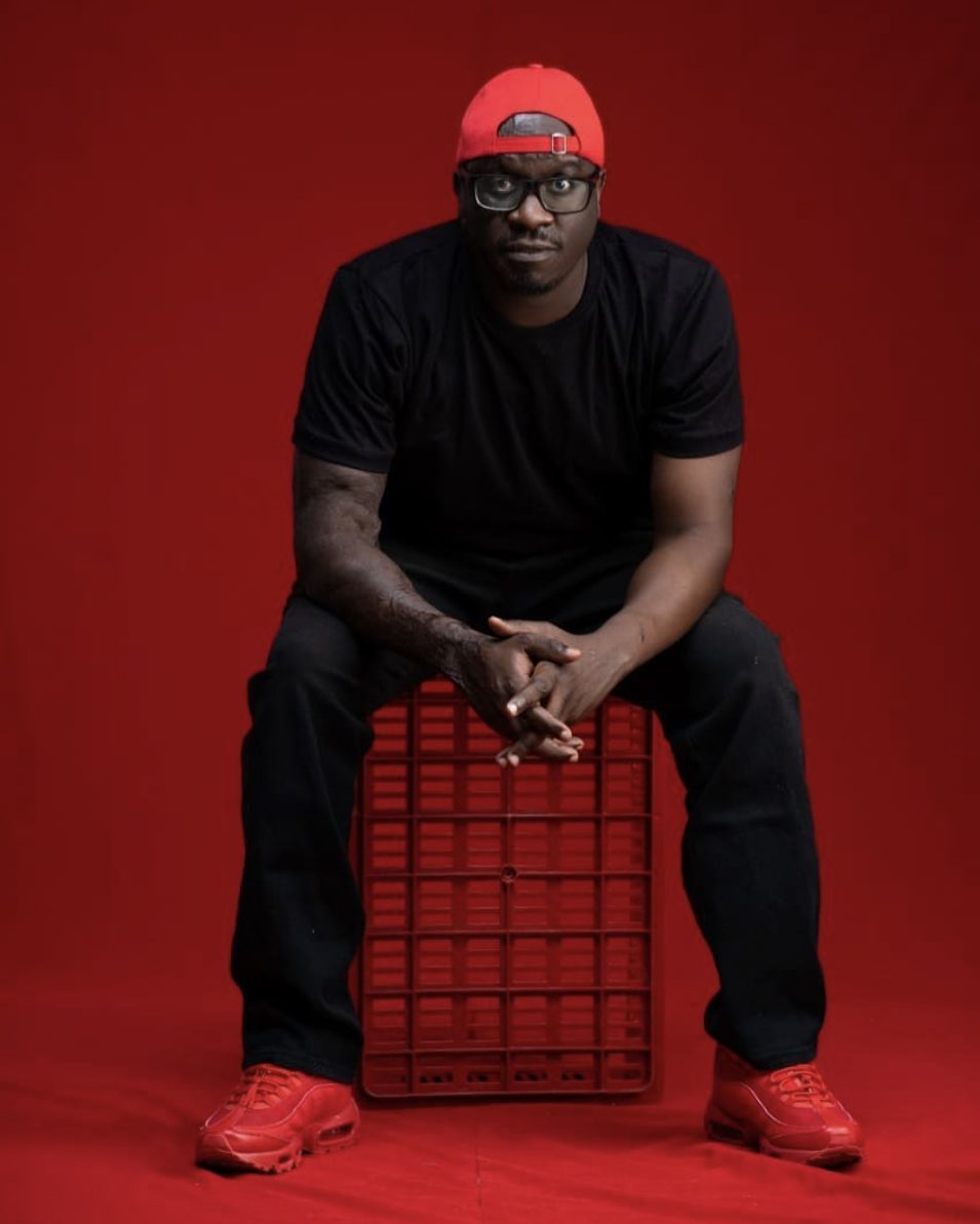 Solodified seated on a red crate against a red backdrop in red and black